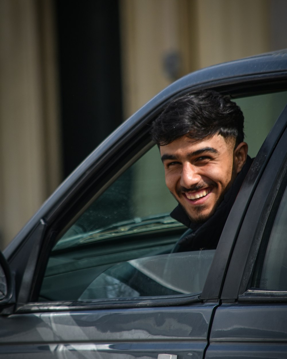 Jovem sorridente dentro do carro, olhando pela janela aberta.