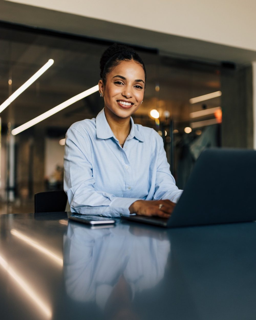 Consultora sorridente diante de um notebook, sentada à mesa em um escritório moderno.